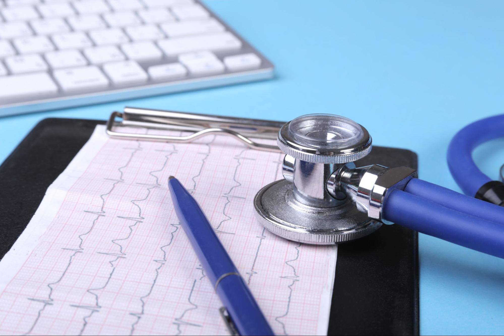 Záznam EKG srdce na papíře s modrým perem a stetoskopem na stole